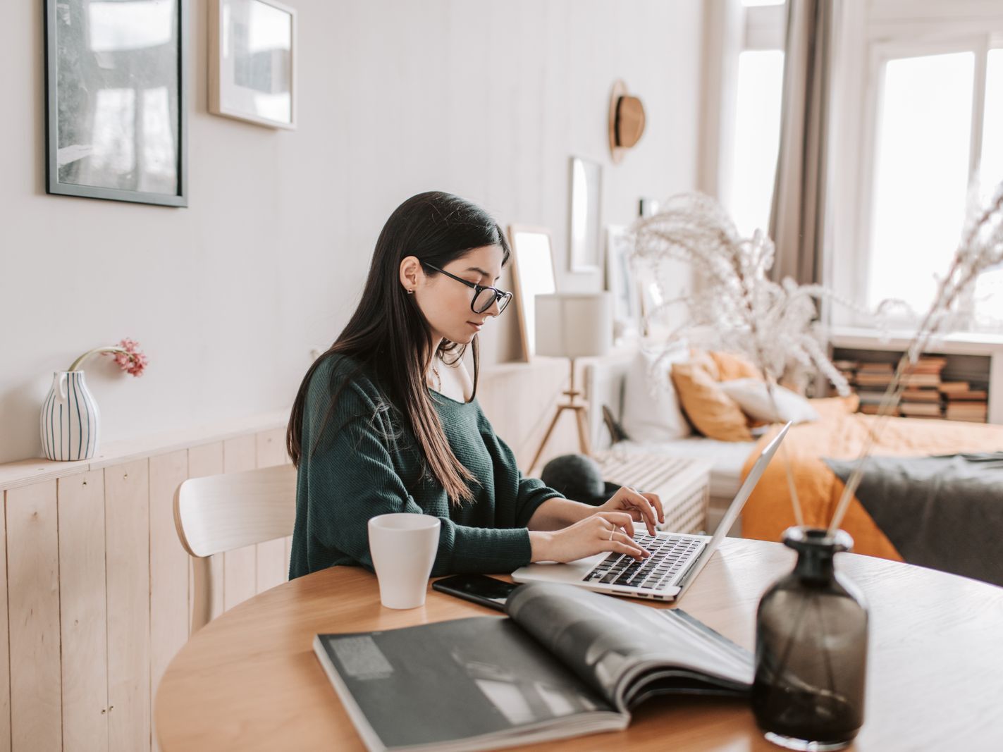 Een freelancer werkt op een laptop aan een ronde tafel in een lichte kamer.