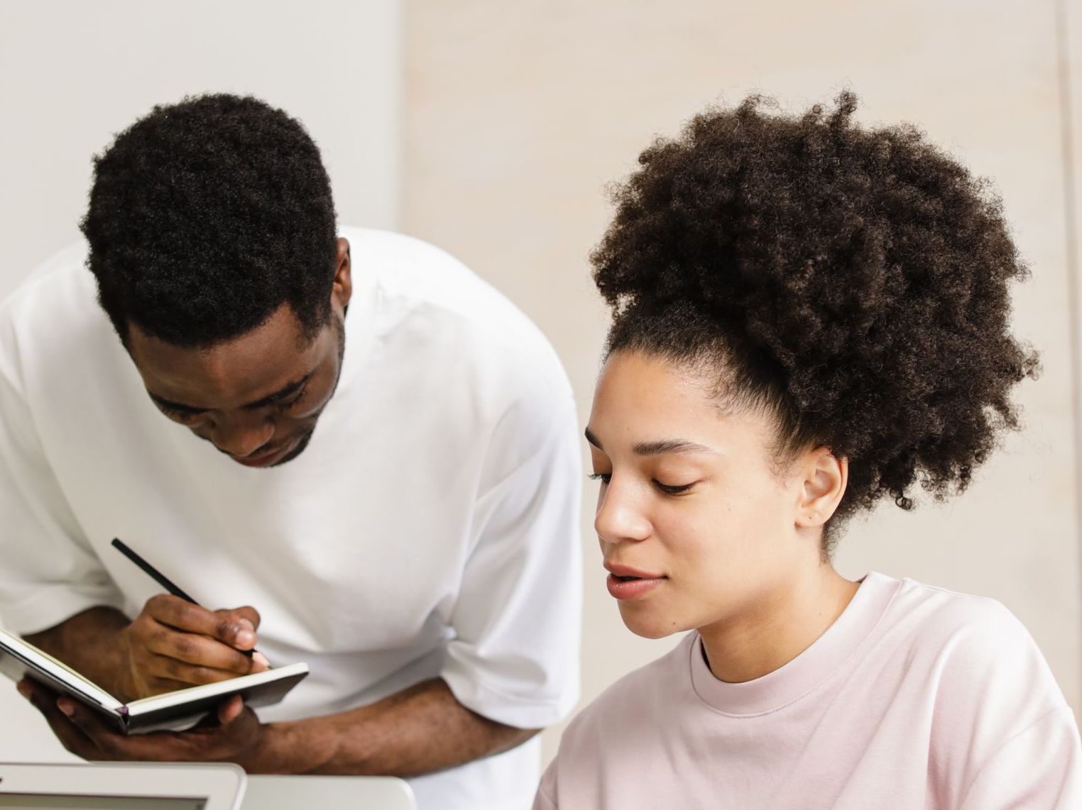 Twee collega's overleggen aan een werktafel; een van hen schrijft in een notitieboek.